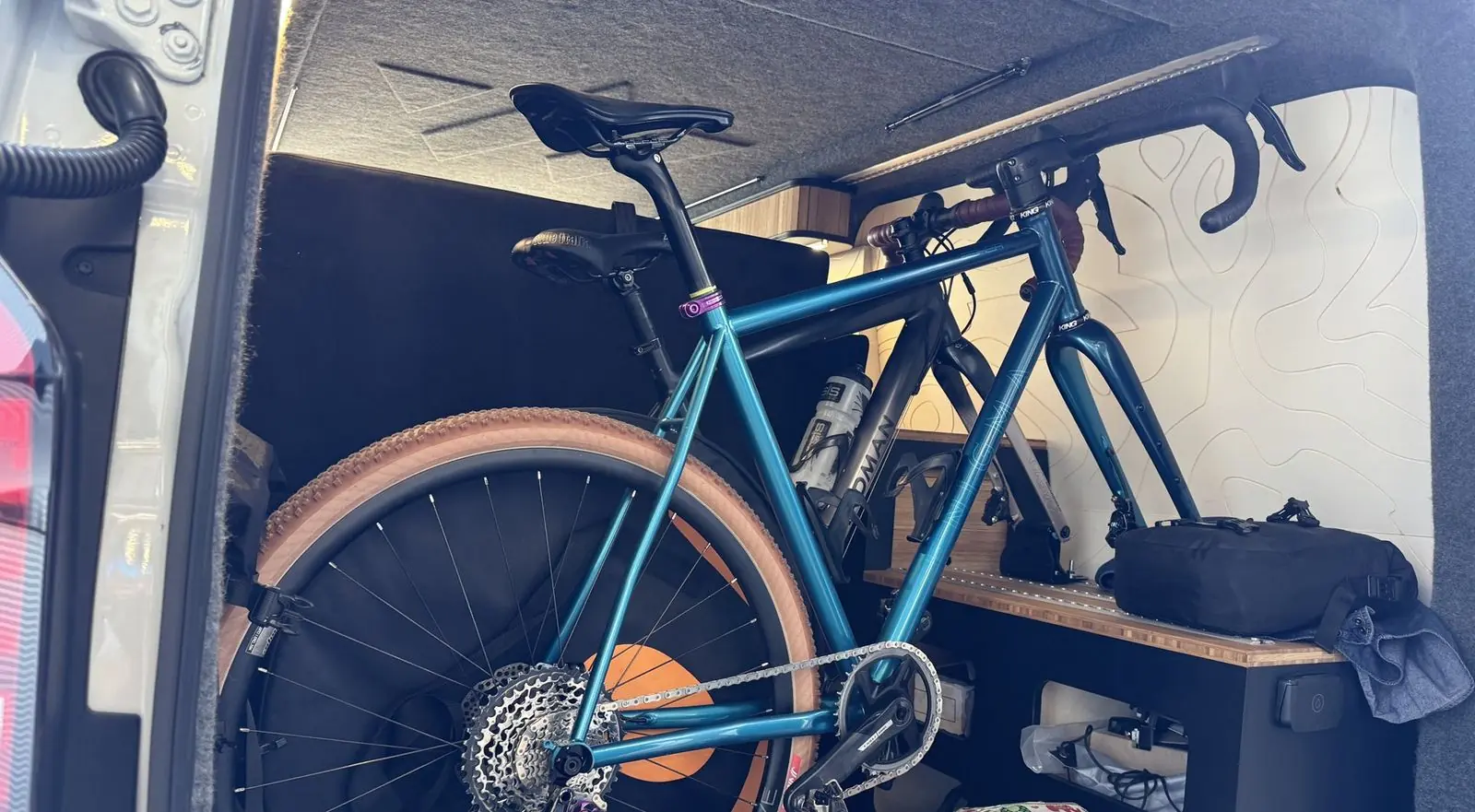 Two bicycles standing upright in the rear of the van behind the seat, beside the black storage unit with its bamboo top.
