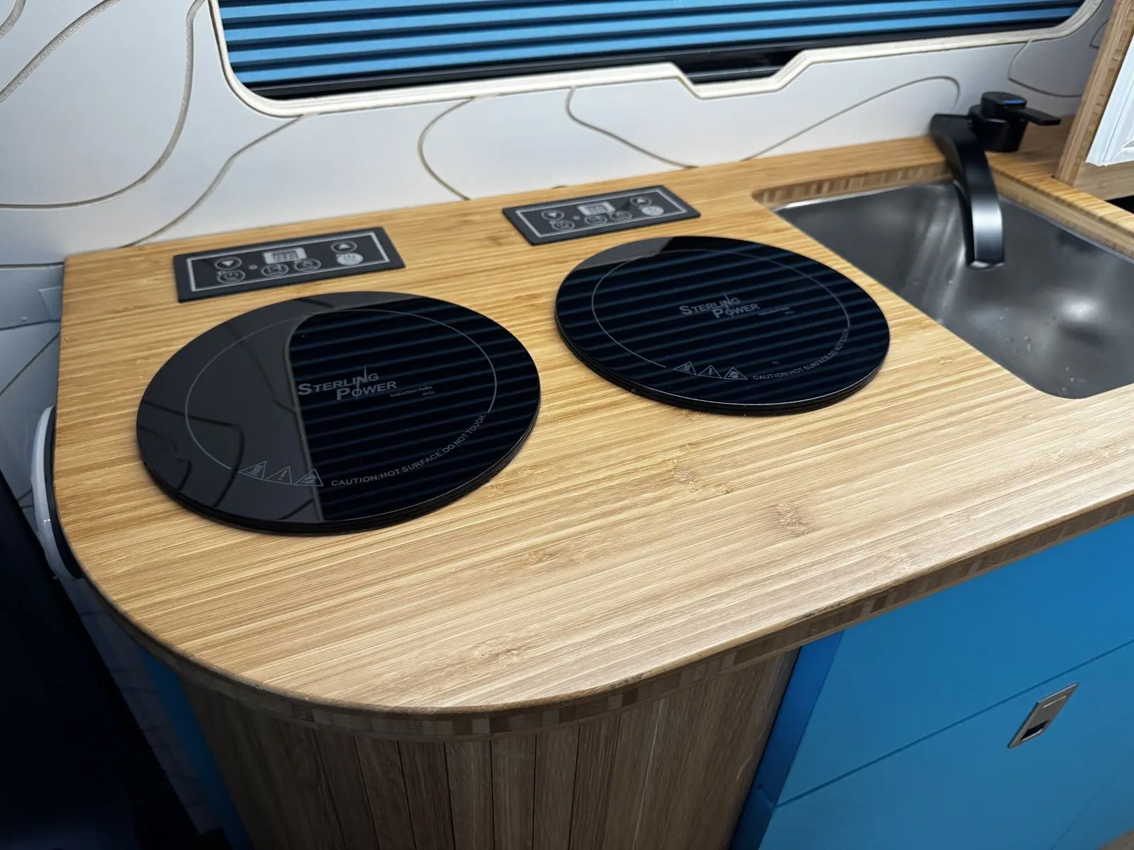 Two round black Sterling Power induction hobs with touch controls set into a bamboo worktop with a rounded end, beside a stainless steel sink with a black tap.