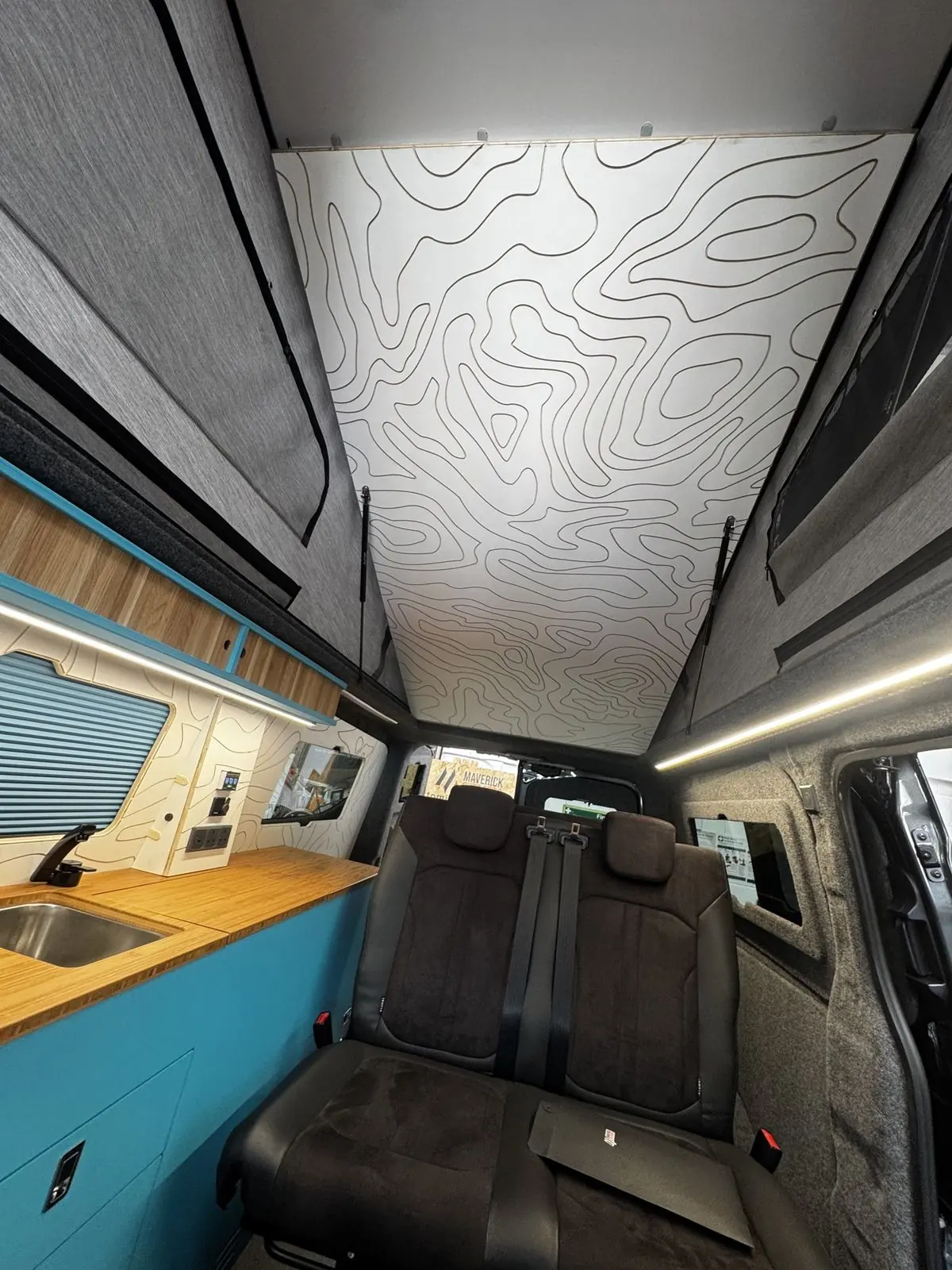 Looking up at the white ceiling panel engraved with contour lines inside the raised pop-top, with grey canvas sides and the black rear seat below.