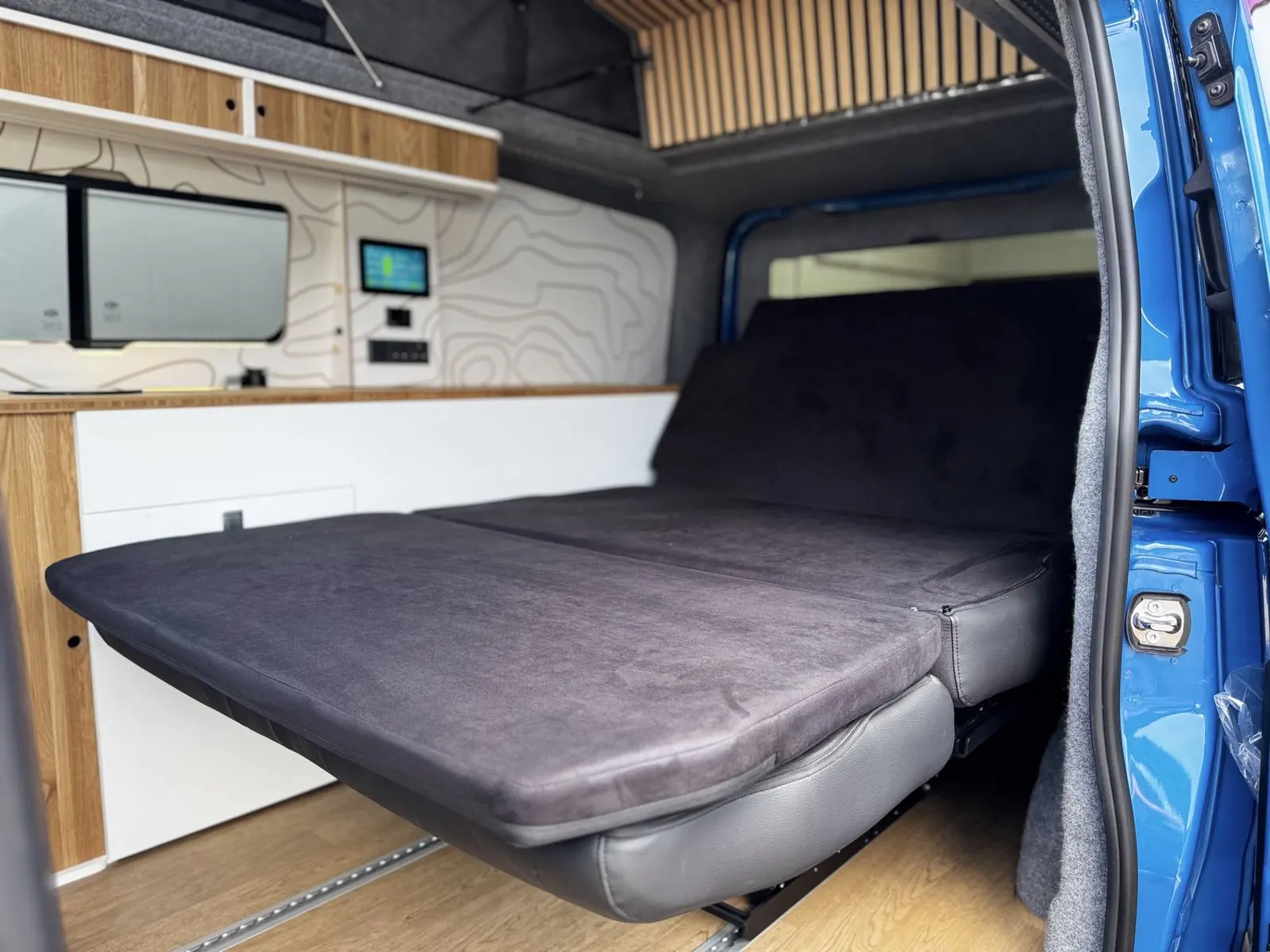 Rear seat folded flat into a bed in black suede-effect fabric, beside the white kitchen unit.