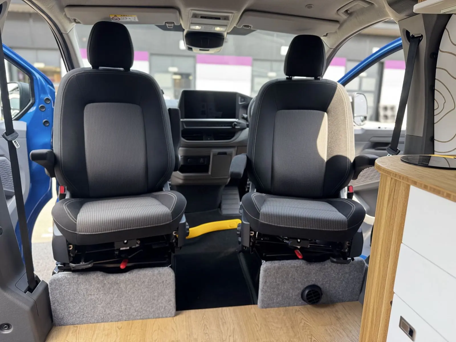 Two front seats in grey and black fabric on swivel bases with carpet-trimmed plinths, seen from the living area.