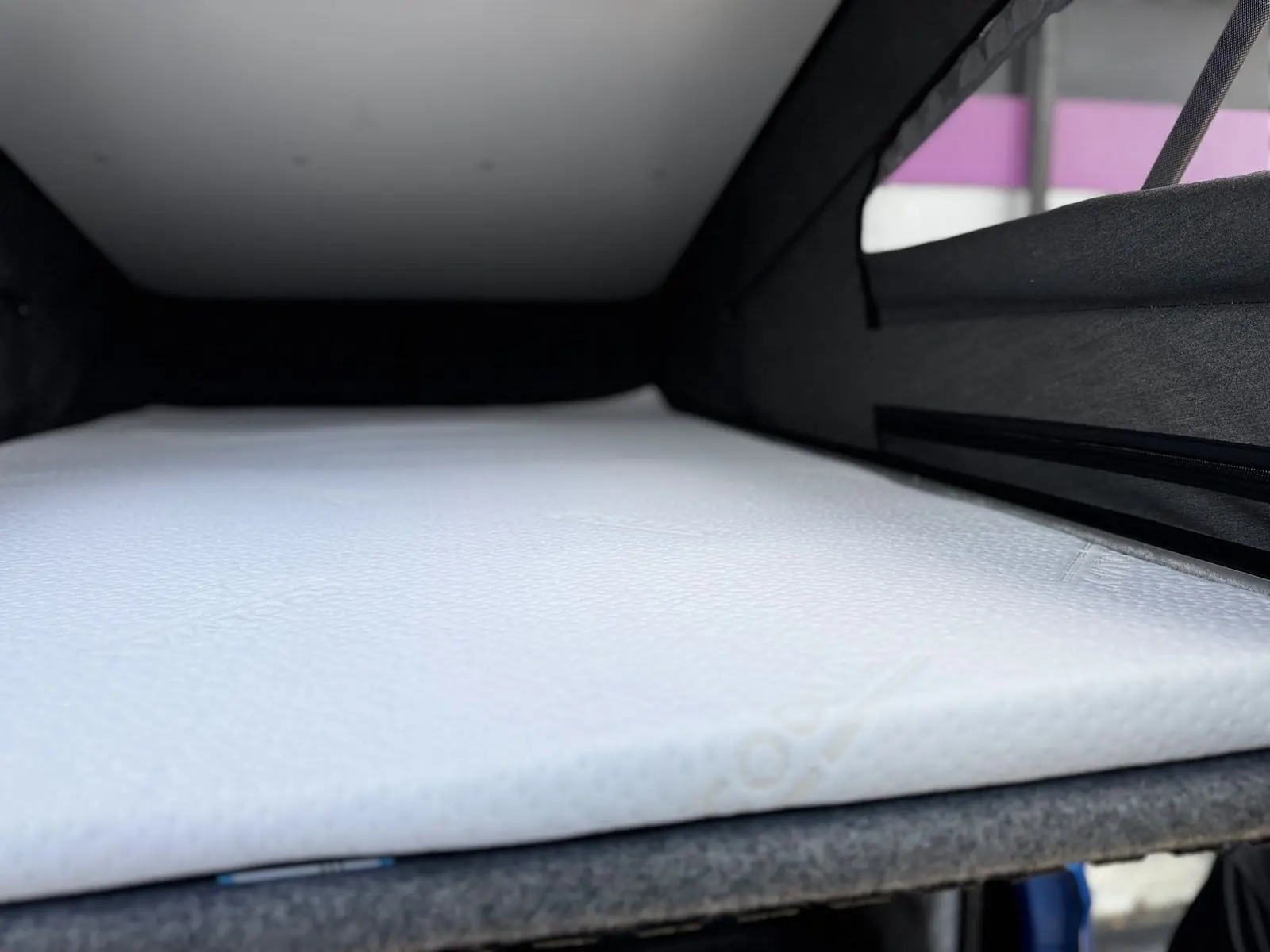 White mattress on the bed platform inside the raised pop-top roof, with dark grey canvas sides.