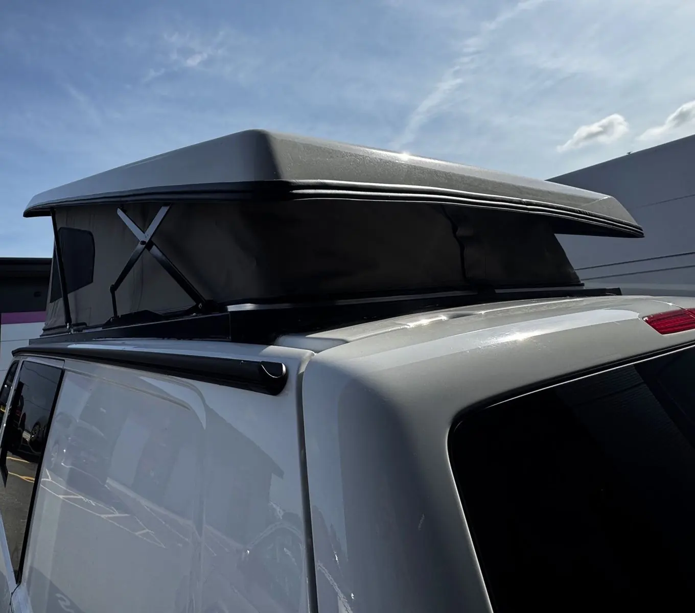 Close view of the raised pop-top roof from the rear corner, showing a silver-grey roof shell and dark canvas with scissor hinges.