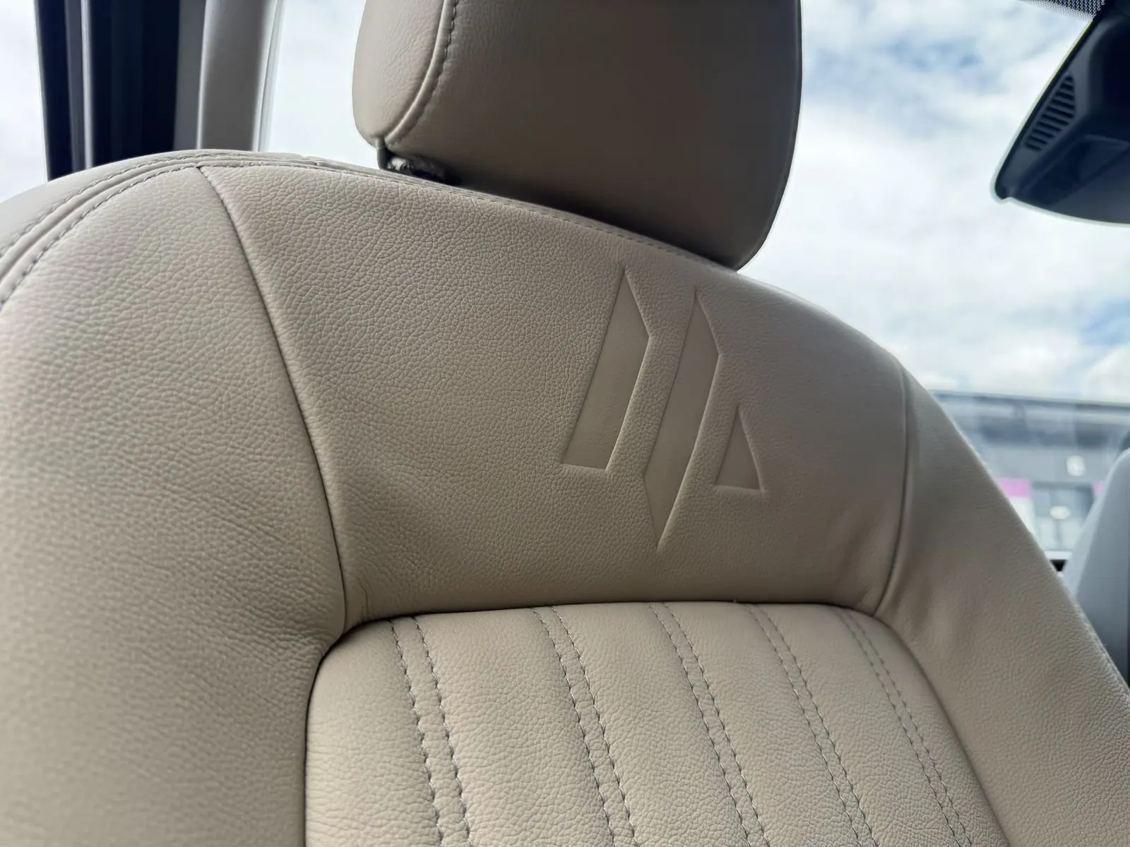 Close-up of a cream leather seat back with the Maverick Outdoors logo embossed below the headrest and vertical stitched panels.