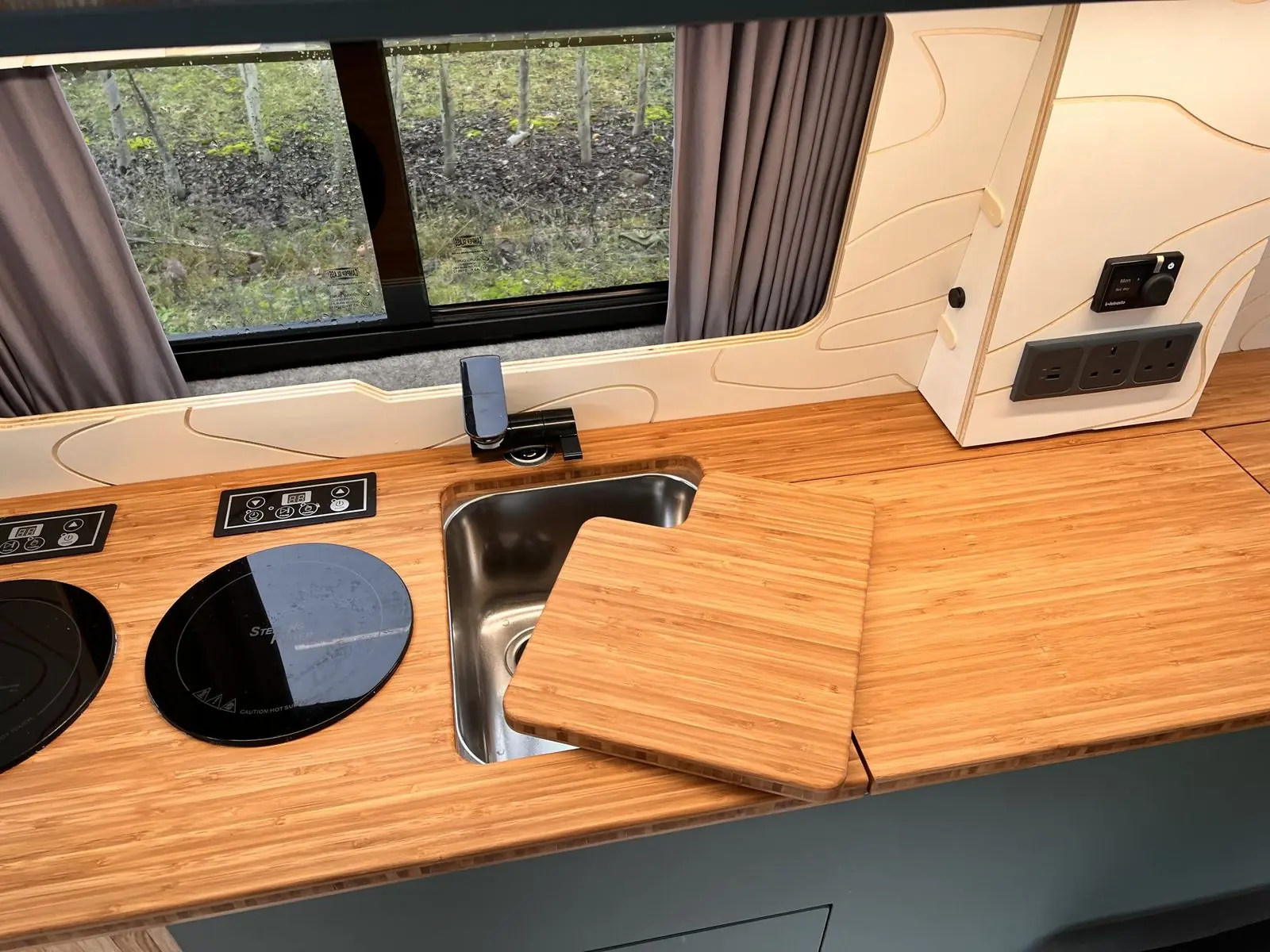 Bamboo worktop with the sink cover lifted to show a stainless steel sink, two round induction hobs with touch control panels and a black tap.