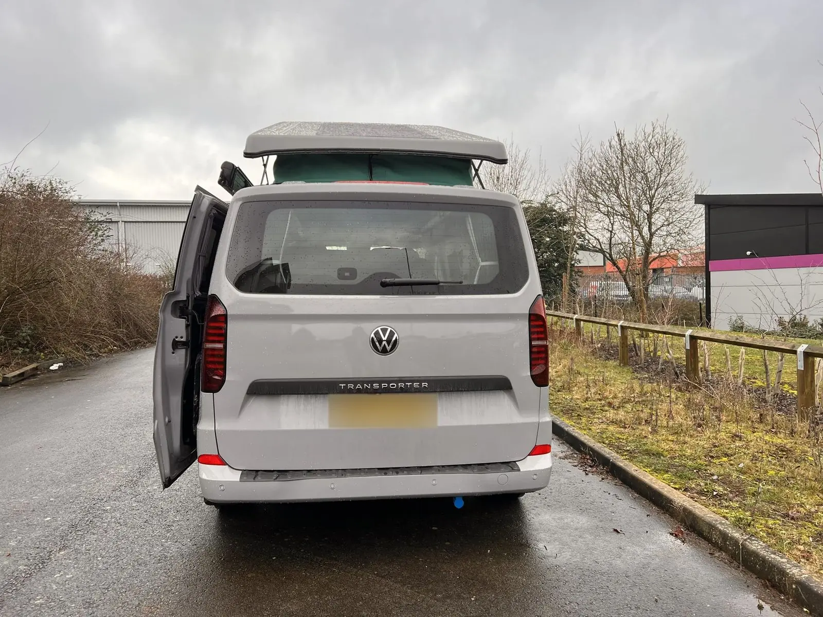Rear view of the light grey campervan with a tailgate and the pop-top raised, with the side door open.
