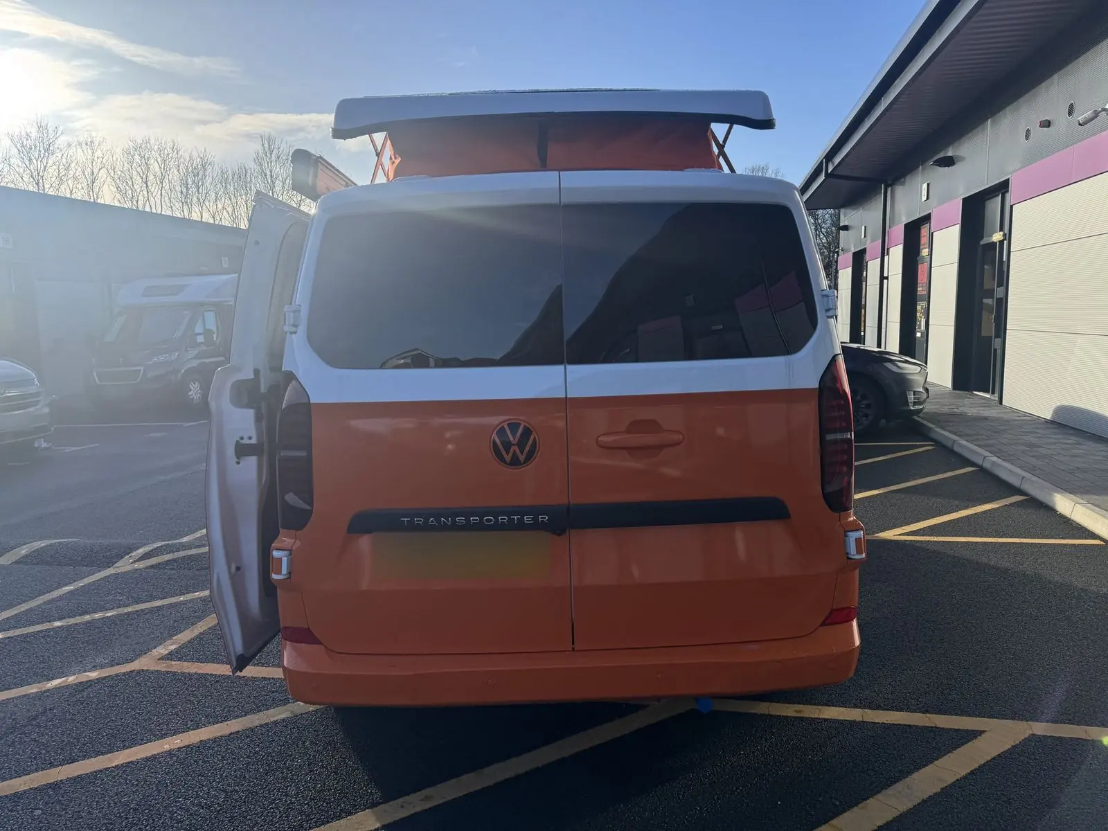 Rear view of the campervan showing white-over-orange barn doors with tinted windows and the pop-top raised.