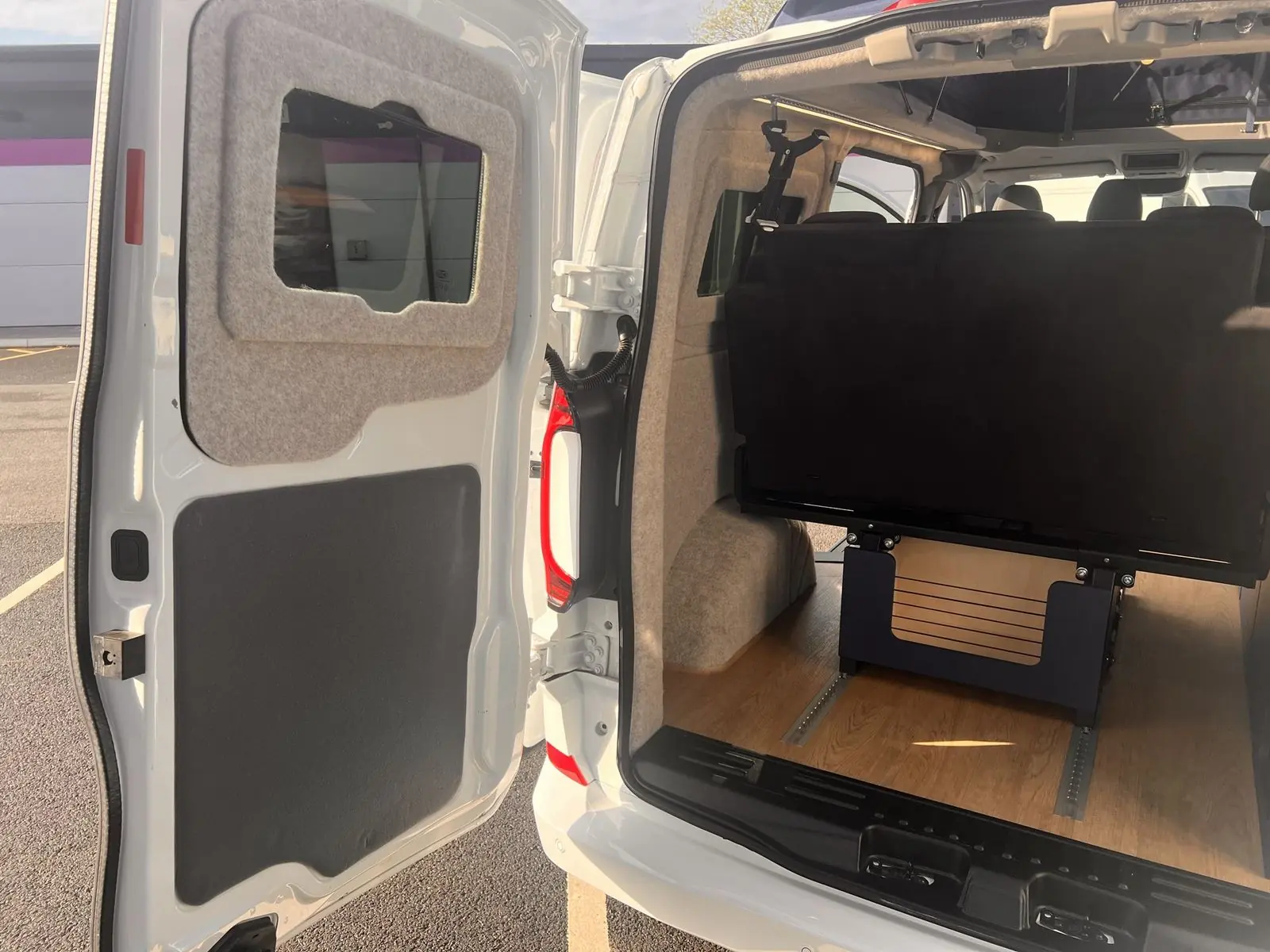 View in through an open rear barn door showing the back of the rear seat, carpet-lined door panel and wheel arch, oak-effect floor and floor rails.