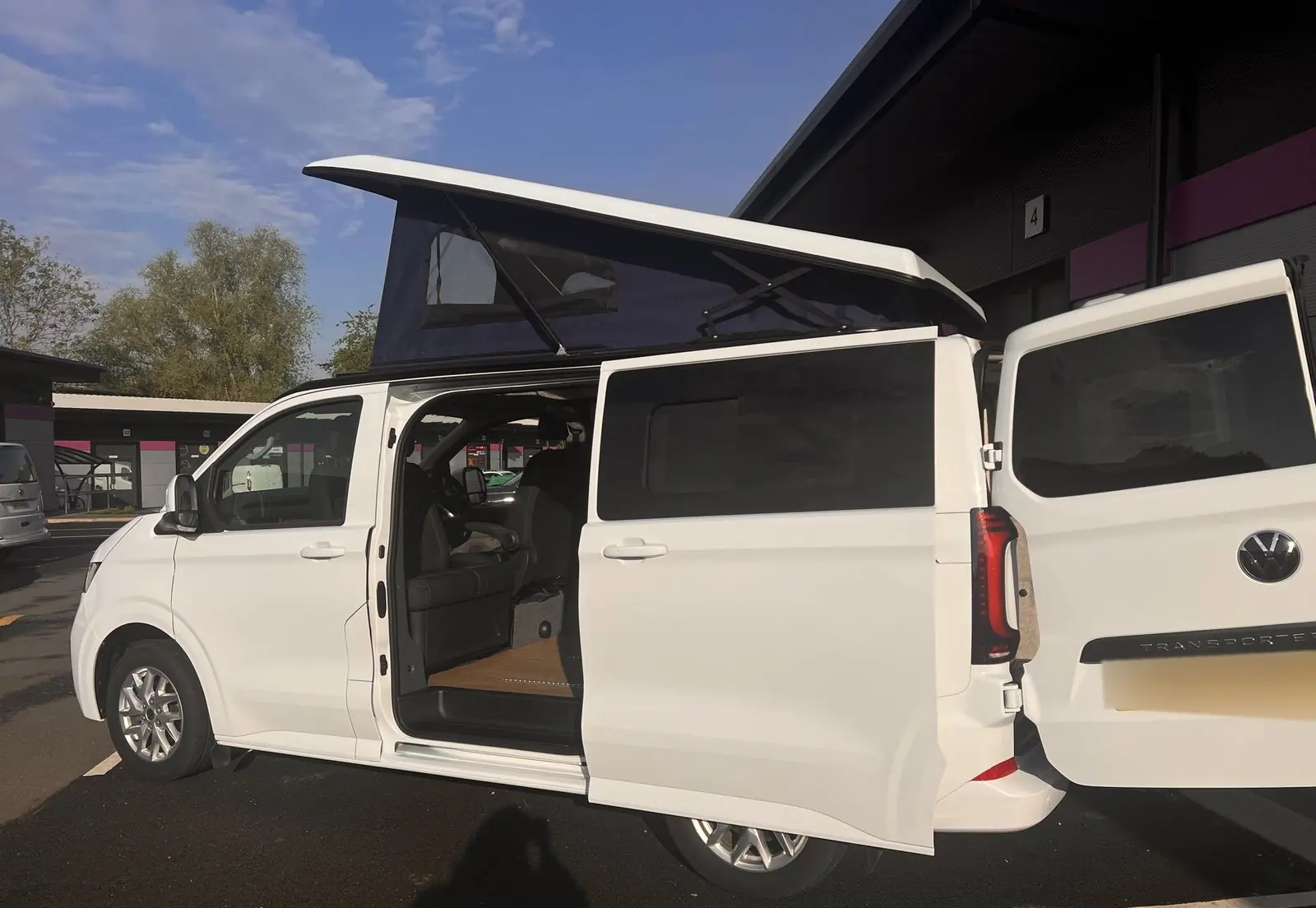 Side view of the white campervan with the sliding door and a rear barn door open and the navy pop-top raised.