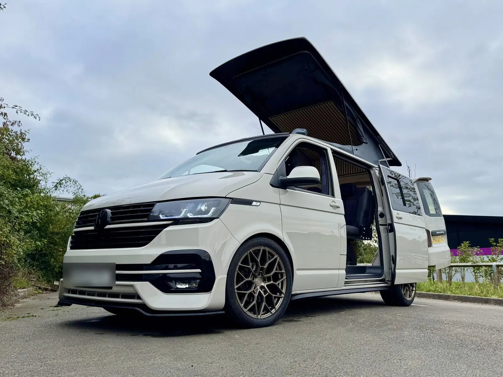 Pale grey camper with bronze wheels, pop-top raised and side door open