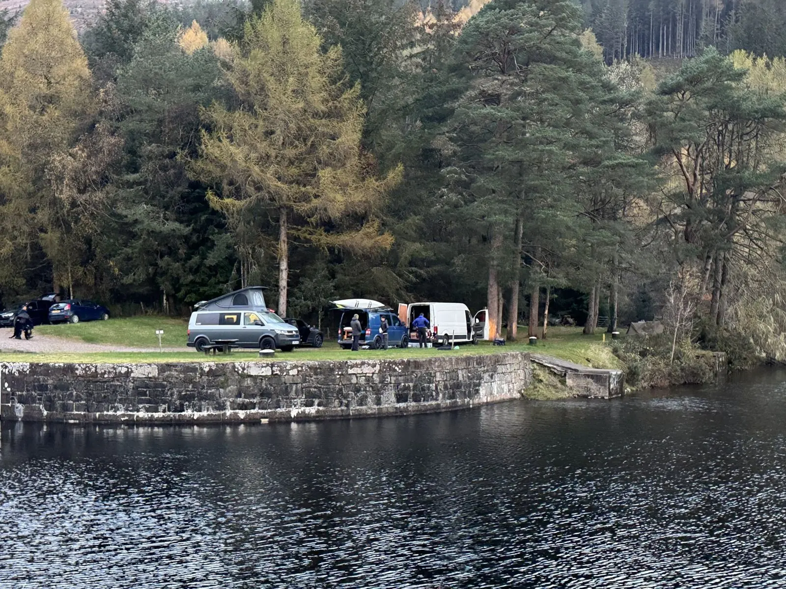 A Maverick camper with its pop-top up on a stone quay beside a loch, pine trees behind