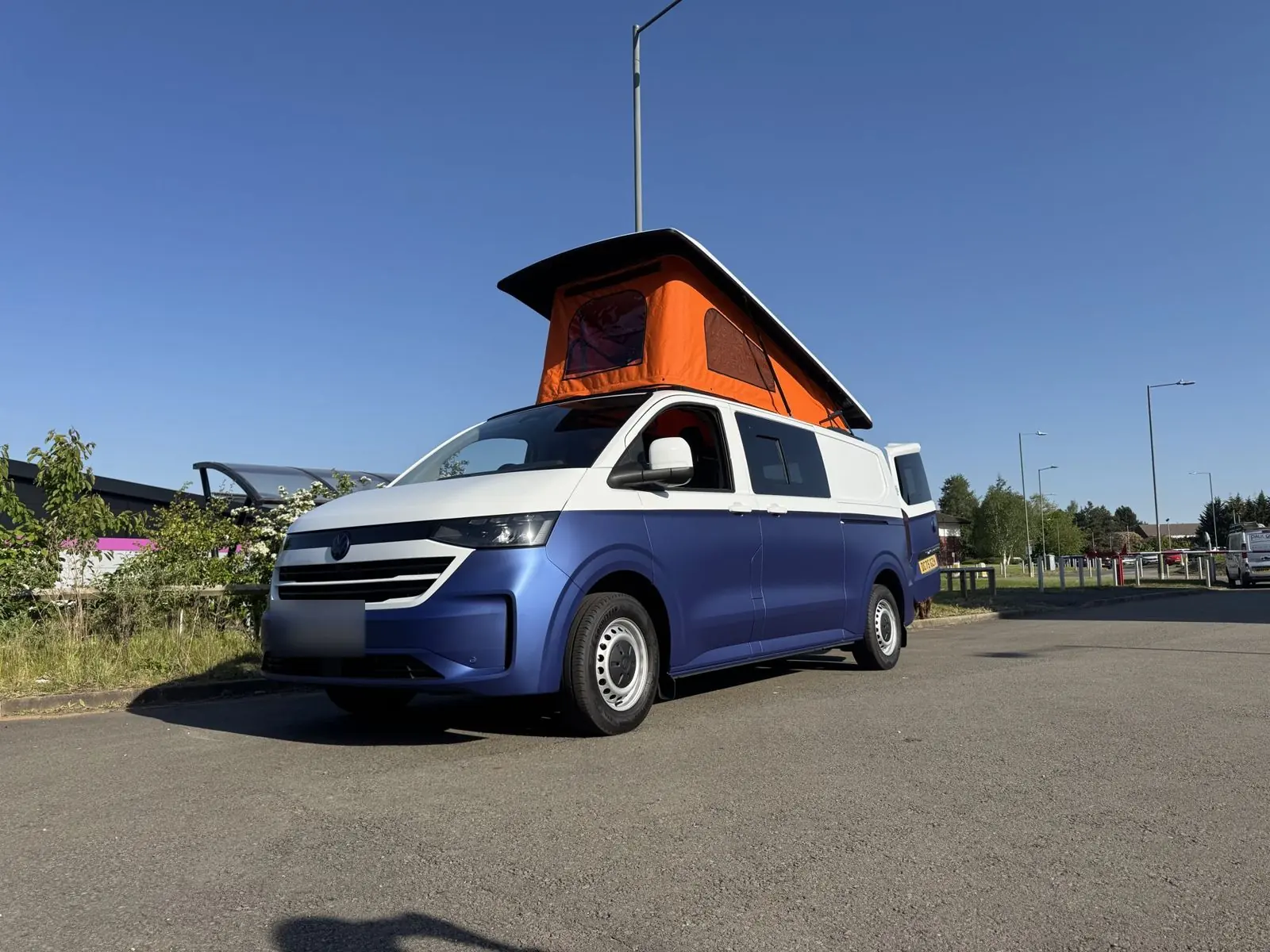 Blue and white two-tone camper with an orange pop-top under a clear sky