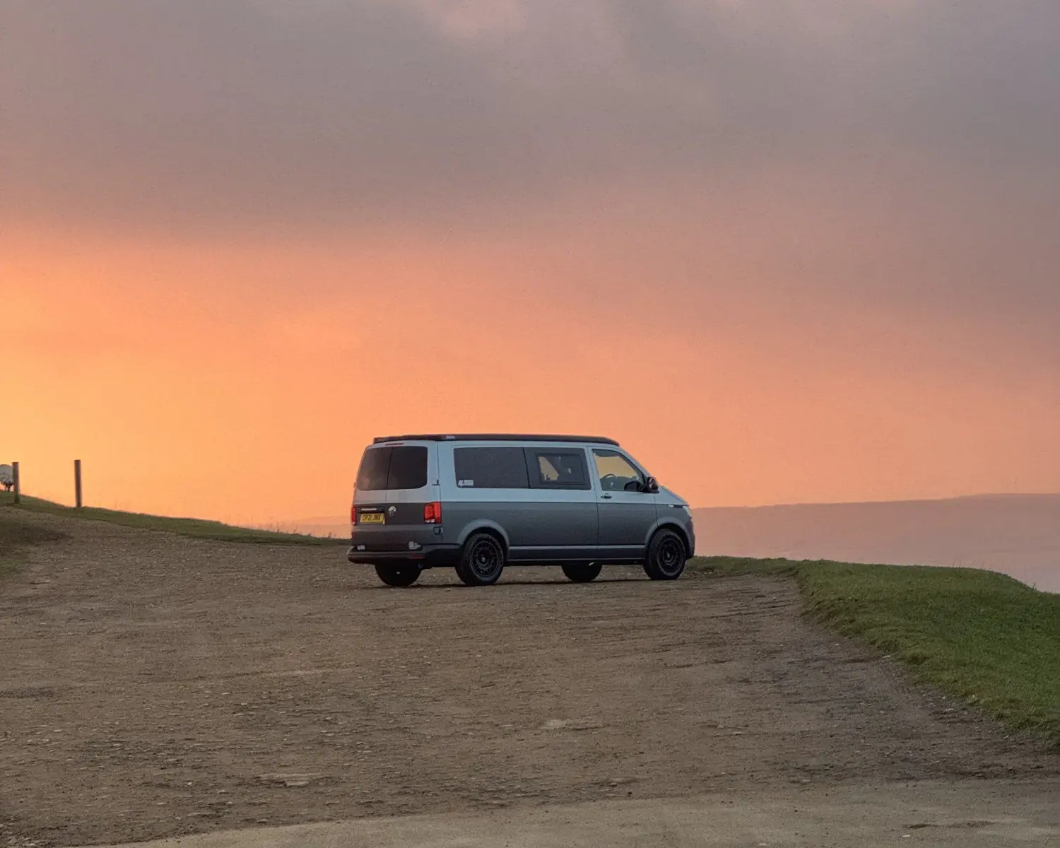A camper parked on a ridge under an orange and pink sunset sky