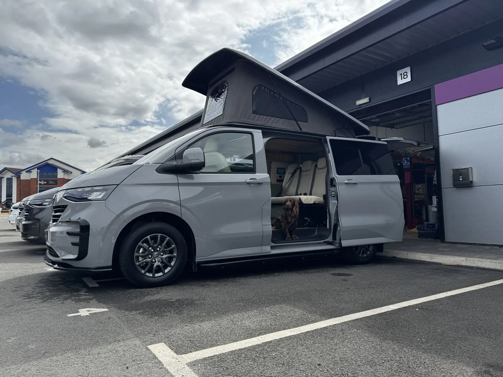 A light grey Maverick camper with its pop-top raised outside the workshop at Unit 18