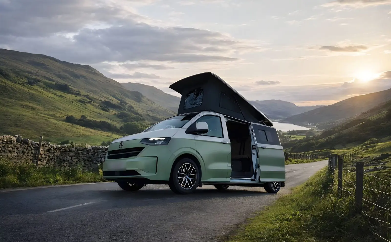 A pale green Maverick camper with its pop-top up on a lane above a valley at sunset