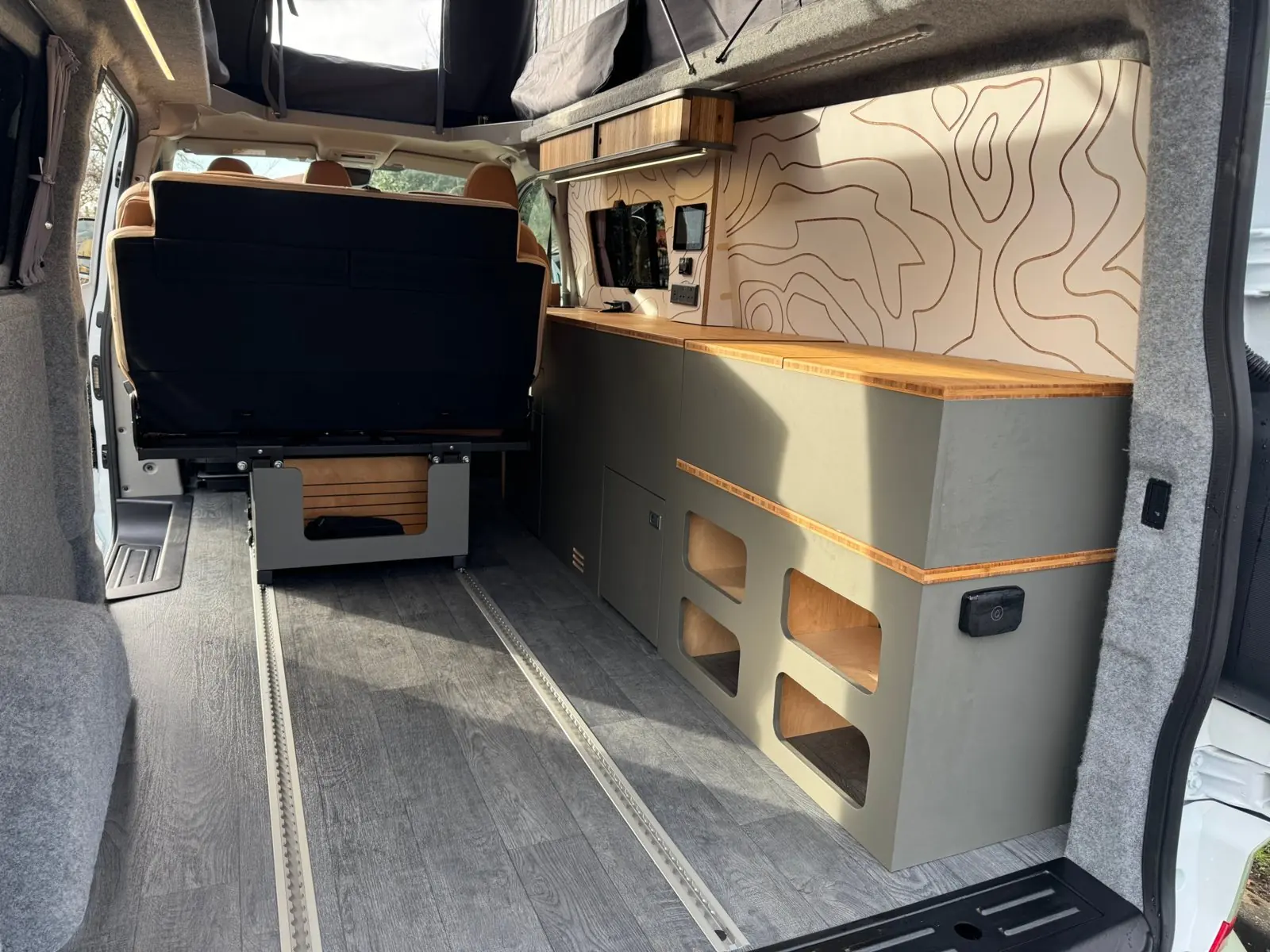 Overland module seen through the rear doors: a grey-green storage cube with open cubbies and a bamboo top, continuing the kitchen run along the wall