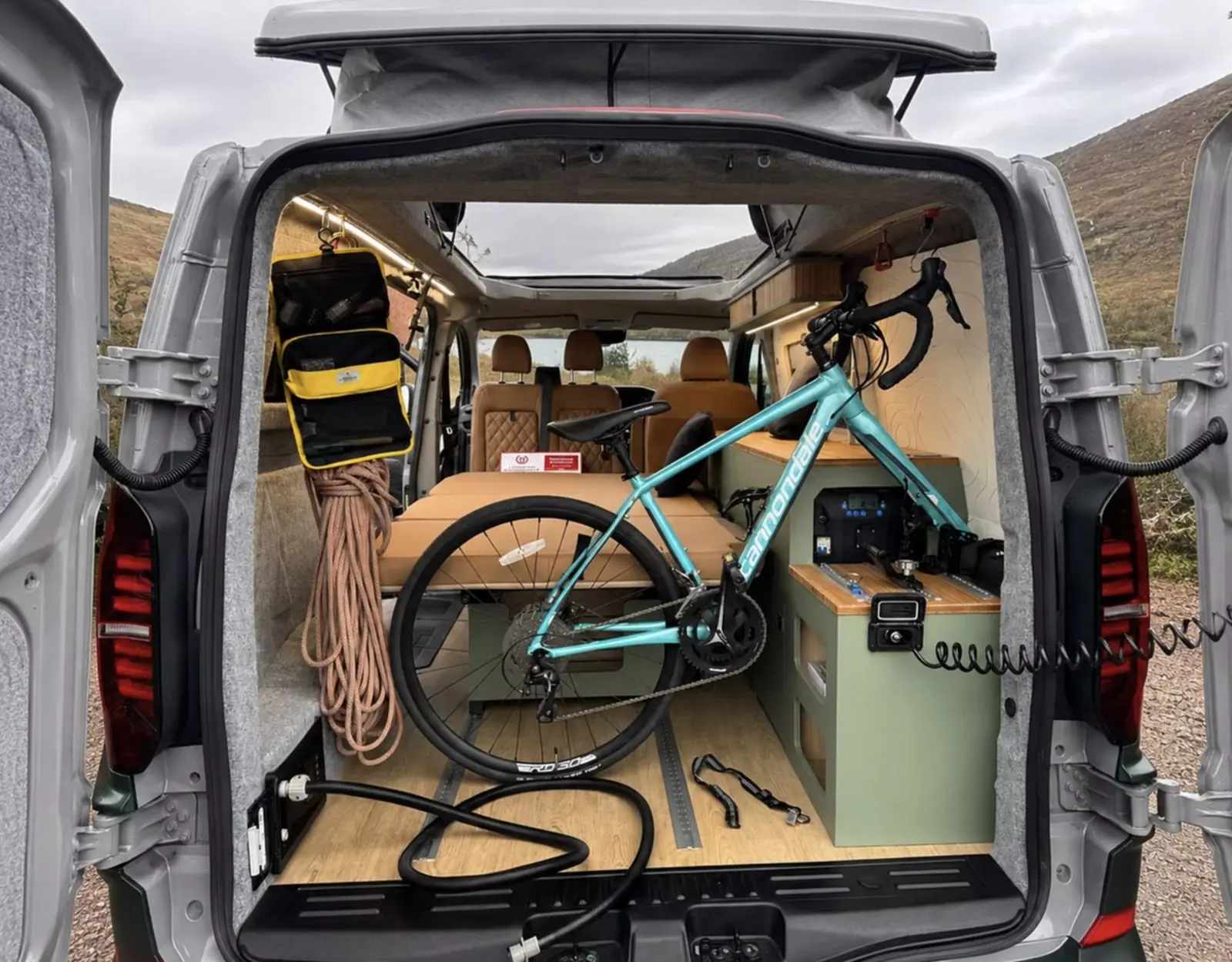 Rear doors open on a Maverick camper by a loch, with a road bike, rope and kit loaded behind the bed