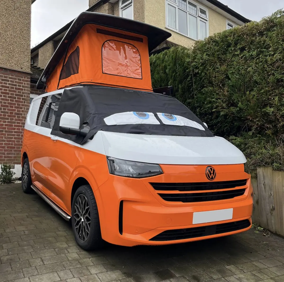 Orange and white two-tone VW Transporter camper with a matching orange pop-top raised, parked on a driveway