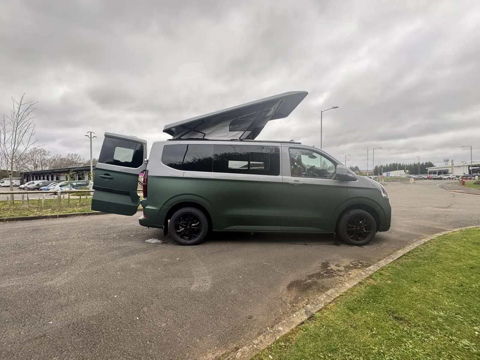 Matt green and silver camper in profile with the pop-top up and a rear door open