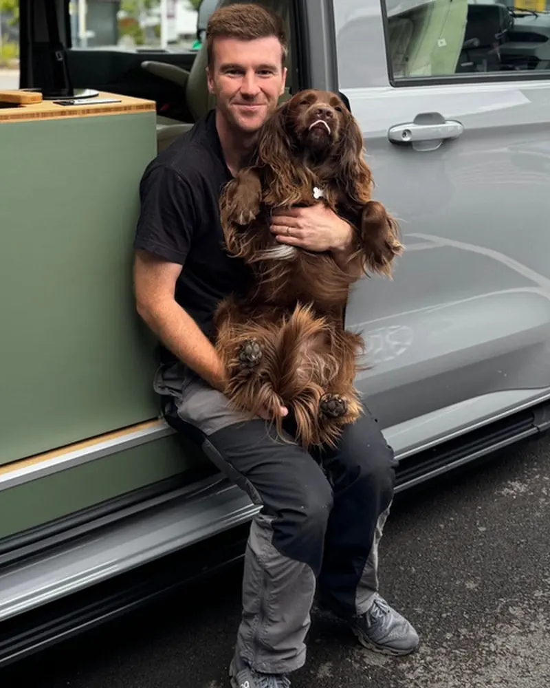 Toby Webb, founder of Maverick Outdoors, sitting in a camper doorway holding Maverick the sprocker