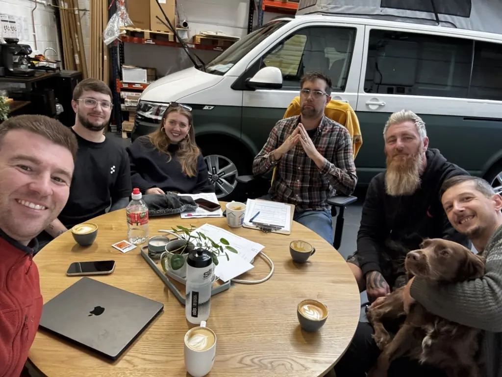 The Maverick Outdoors team around a table in the Warwick workshop with coffees, and Maverick the sprocker, in front of a green and white VW camper